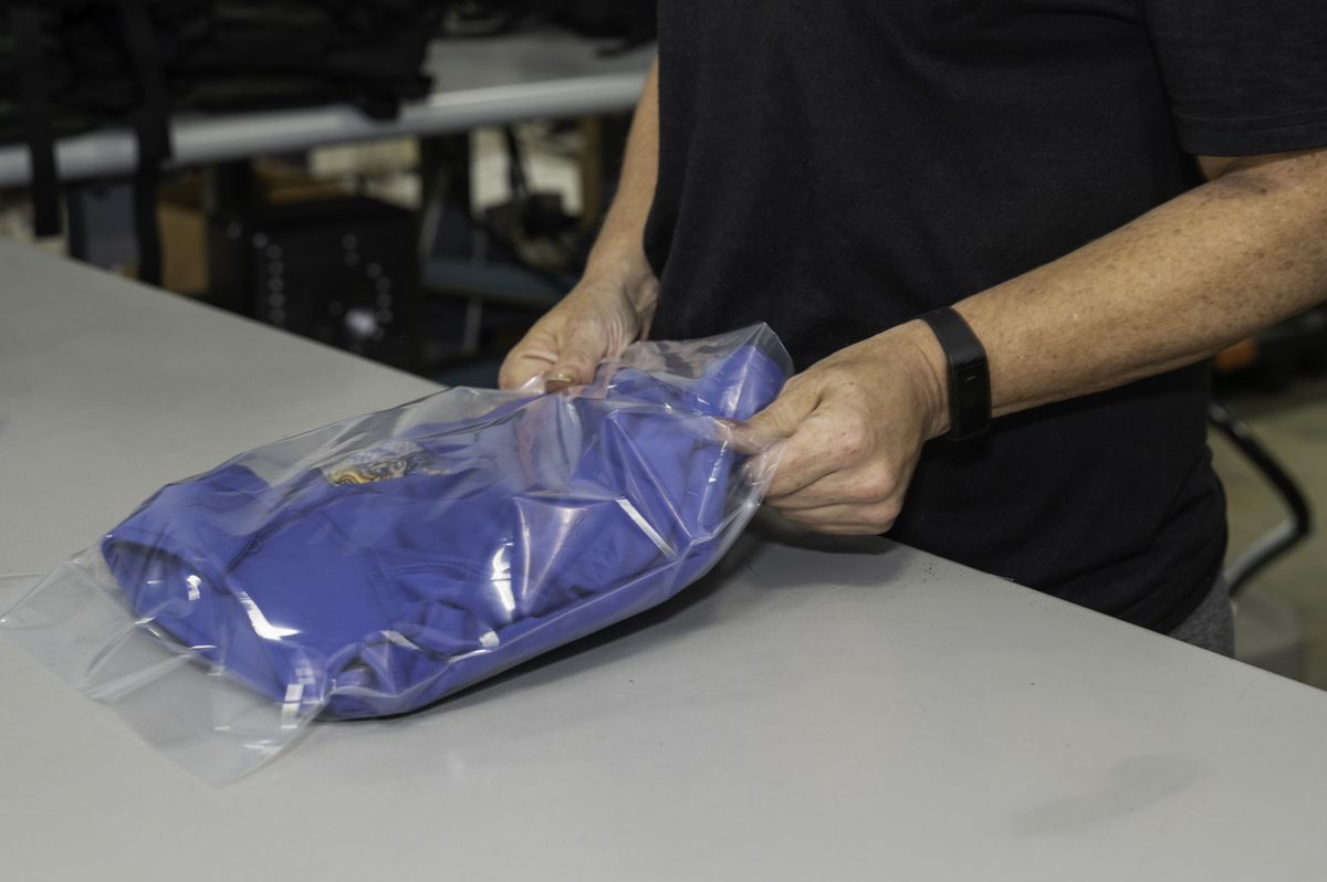 someone packaging a blue shirt in a clear bag